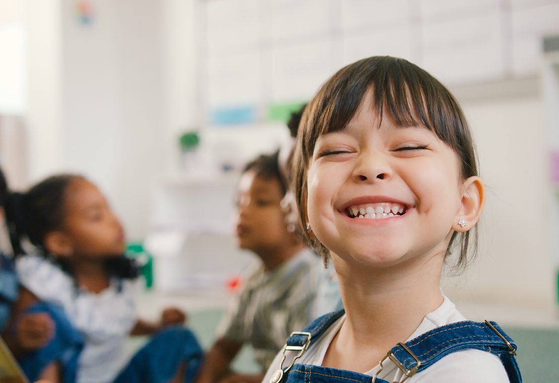 A smiling school-age child in a classroom, illustrating children's dentistry at Aesthetic Dentistry